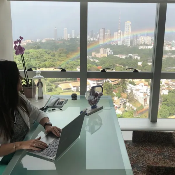 Dra. Sabrine Vilán no consultório, com vista para Salvador e um arco-íris