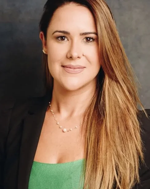 Dra. Sabrine Vilán sorrindo, de blazer preto e blusa verde